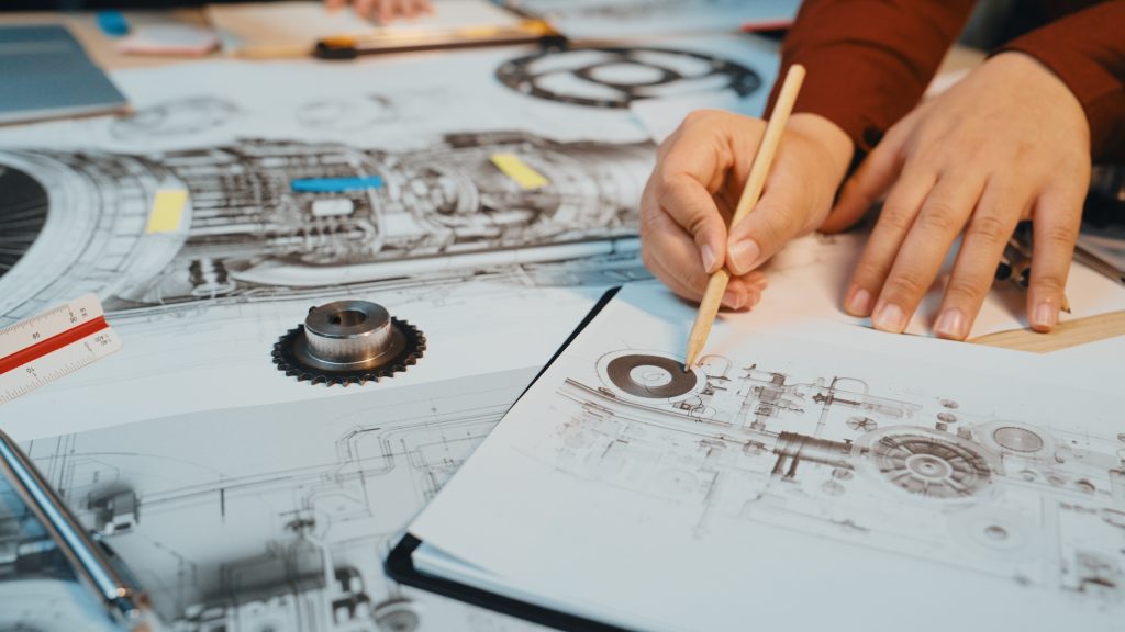 echnical-drawing-design-sketches-machinery-components-workspace-with-hands-holding-pencil-creative-engineering-environment-sactr-scaled